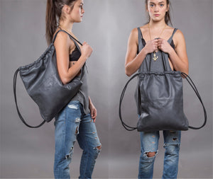 Gray multi-way leather drawstring backpack crafted with soft Italian Napa leather, adjustable back straps, and leather-covered inner top handles. This style is versatile and can be carried as a backpack, tote, or on the shoulder. Its ideal minimalist design is suitable for long active days & use. Suitable for laptops up to 15inch.